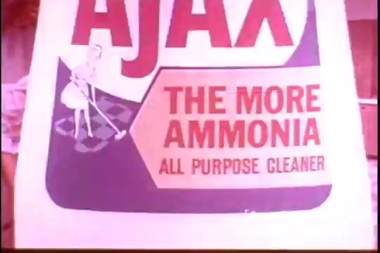 The still features a vintage advertisement for Ajax, highlighting its cleaning product with an eye-catching design. The bold red and blue text reads 'AJAX' at the top, followed by 'THE MORE AMMONIA' and 'ALL PURPOSE CLEANER' in prominent lettering. An illustration of a woman cleaning reinforces the message. The overall aesthetic reflects mid-20th century advertising styles, emphasizing effectiveness and household cleanliness.