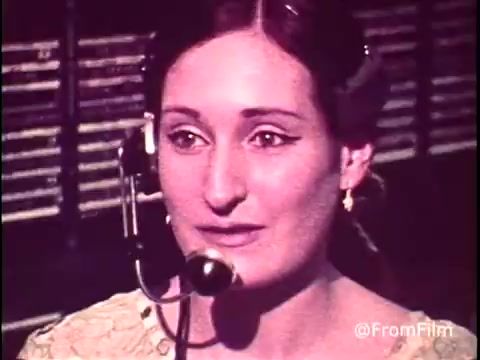 In this still from the early 1970s C&P Telephone commercial, a female telephone operator is featured, engaged in her work at a cord switchboard. She wears a vintage headset, indicating her role in facilitating long-distance calls. The background reveals rows of cord connections, emphasizing the technology of the time. Her expressive gaze suggests attentiveness and professionalism, highlighting the human aspect of communication before modern technology. Follow @FromFilm on Twitter for more insights!