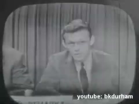 The 16mm still captures a moment from a 1950s Kinescope, likely showcasing a San Diego-based religious TV show. The image features a presenter at a desk, indicating an interview or discussion format typical of the era. The monochrome aesthetic, characteristic of early television, adds to the nostalgic feel of this broadcast. The context suggests a likely emphasis on faith-related topics relevant to the audience at that time.