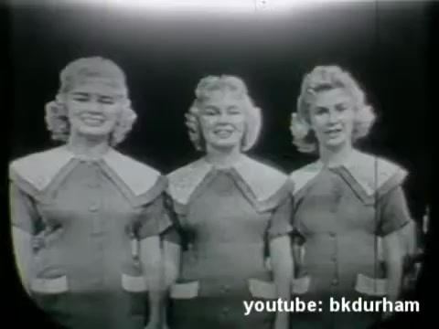 The still features three women dressed in matching outfits, likely from a 1950s religious TV show. They display cheerful expressions and are posed together, indicative of the era's television aesthetic. The black-and-white quality suggests it was captured on 16mm film, typical for kinescope broadcasts of that time. This context implies a focus on community and faith, common themes in religious programming during the 1950s.