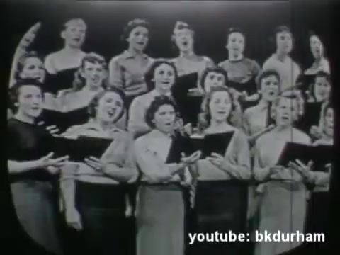 The still shows a choir of women performing, likely in a religious context as part of a 1950s Kinescope broadcast from a San Diego-based TV show. The singers appear to be wearing matching attire and are actively engaged in their performance, suggesting a communal or worshipful atmosphere. The production likely reflects the era's style, featuring live broadcasts of religious content that aimed to reach audiences in their homes.
