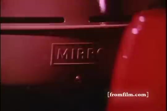 The still from the 'Mirro Broiler Commercial - 1970s' features a close-up of a cooking appliance, specifically highlighting the 'MIRRO' brand name engraved on the metallic surface. The background is a mix of warm, muted colors typical of the era, suggesting a nostalgic and homey feel. The overall composition emphasizes the product's design, characteristic of mid-20th century kitchenware. The image captures the essence of promotional materials from that time.