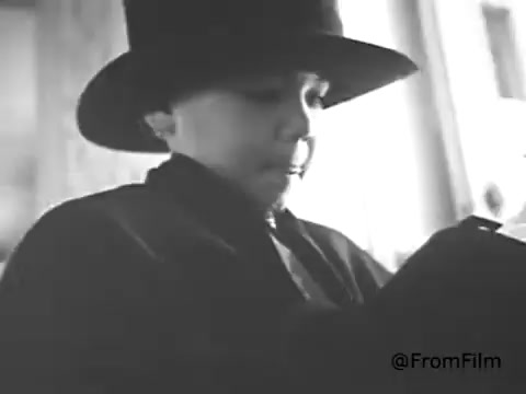 The still from the American Cancer Society PSA (1968) features a young boy wearing a large hat, seemingly deep in thought or contemplation. The monochromatic tones of the image suggest a serious or somber mood, aligning with the PSA's themes of awareness and prevention related to cancer. The setting appears to be indoors, adding an intimate atmosphere to the scene.