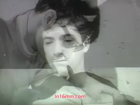 The still from the trailer of 'Out Of It' (1968) features a blurred, dual-image effect. One image shows a young man, possibly in a thoughtful or introspective state, while another appears to depict a person styling or cutting hair. The aesthetic captures a sense of the film's era, hinting at themes of youth and self-discovery. The monochrome look adds a nostalgic quality, typical of trailers from that time.