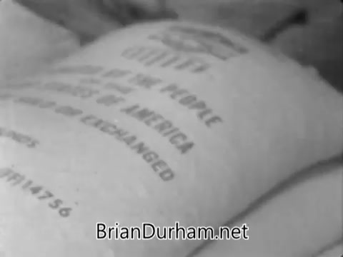 The still from the 'Catholic Bishops' Overseas Aid Fund PSA' shows a close-up view of a burlap sack labeled with text that highlights aid and assistance. The imagery emphasizes themes of charity and support for communities facing food scarcity and high infant mortality rates. This visual reinforces the PSA's message about the growing disparity in resource distribution and encourages viewers to contribute to alleviating this gap through donations to Catholic relief services.