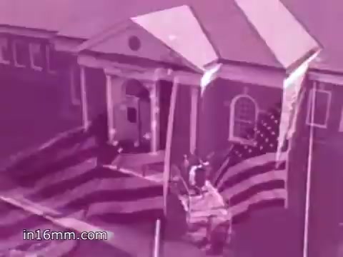 The still from the 1968 PSA features a historical building, likely the American Freedom Center at Valley Forge, draped in large American flags. The scene evokes a sense of patriotism and remembrance, aligning with the voiceover by Anita Bryant as she references the winter hardships faced by George Washington and his army. The overall tone is solemn yet uplifting, reinforcing themes of freedom and brotherhood in America. The image has a pinkish tint, characteristic of certain film stocks from that era.