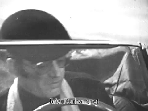 The still from the 1968 Red Rose Tea commercial features a man wearing a bowler hat and sunglasses, seated in a convertible. He appears focused, potentially driving along a scenic route. The background suggests an open landscape, typical of mid-century American visuals. The overall tone conveys a sense of adventure or leisure, complementing the branding of the tea.