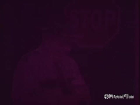 The still from the 1970s PSA 'Save Electricity by Using Reflector Bulbs' features a dimly lit scene where a figure is highlighted in front of a stop sign. The overall mood is somber, indicating a serious tone related to the message about energy conservation. The figure may be seen holding or gesturing toward the reflector bulb, emphasizing its importance in saving electricity.