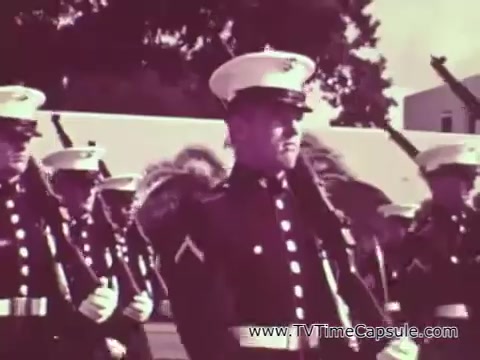 The still likely depicts a formation of U.S. Marines in uniform during the Vietnam era, emphasizing discipline and camaraderie. The Marines are dressed in their formal attire, featuring white service caps, and appear to be engaged in a drill or ceremony. This visual aligns with the themes of the recruiting spot, which aims to showcase the transformation and character development associated with Marine Corps training. The overall tone suggests strength, unity, and dedication.