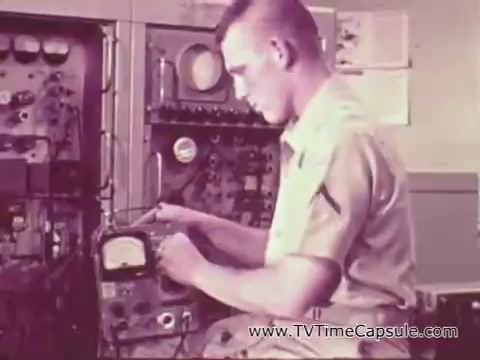 In this 16mm still from the Vietnam-era Marine Corps recruiting spot titled 'The Marine Corps Builds Men,' a young Marine is focused on operating a piece of electronic equipment. He is dressed in a military uniform, showcasing a technical or engineering role. The background features various gauges and dials, highlighting the technical skill set involved in the Marine Corps. The image emphasizes training and discipline, portraying a sense of pride and dedication.