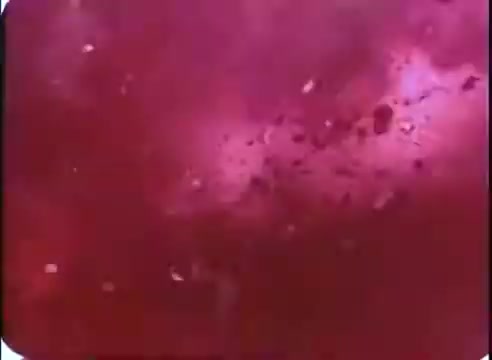 The still from ''The Time Machine' - promos' features a vibrant, swirling mass of red and purple hues, creating an abstract, dynamic backdrop. It evokes a sense of motion and perhaps the passage of time, fitting the film’s theme. The texture appears granular, characteristic of a 16mm print, enhancing its retro aesthetic.