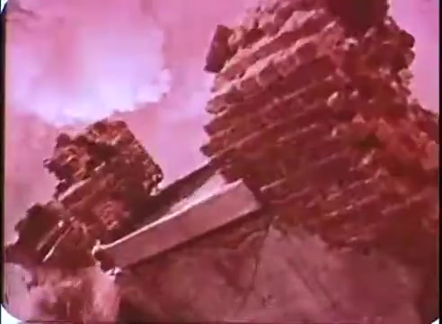 The still from 'The Time Machine' promos features a surreal, desaturated depiction of crumbling brick structures. The background is a soft, pink-hued sky, creating an ominous atmosphere that suggests desolation and decay. The focus on the ruins emphasizes themes of time, change, and the remnants of civilization.