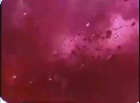 The still from 'The Time Machine' promos presents a vibrant, abstract background with swirling shades of deep red and hints of purple. It appears to evoke a sense of movement and energy, likely representing the idea of time travel or a swirling time vortex, consistent with themes from the film. Fragmented light spots are scattered throughout, adding to the dynamic atmosphere.