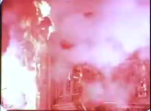 The still from 'The Time Machine' promos depicts a dramatic scene featuring intense flames and smoke, creating a sense of chaos and urgency. The vibrant colors suggest a high-stakes moment, potentially related to destruction or a pivotal event in the narrative. The setting appears to be an elaborately designed structure, hinting at a futuristic or historical context.