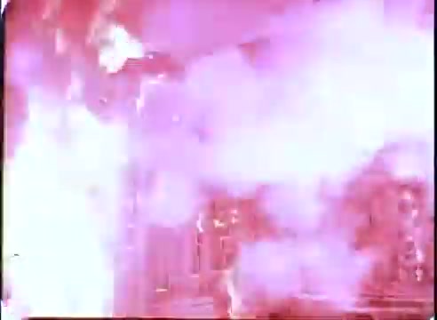 The still from 'The Time Machine' promos depicts a dramatic scene filled with intense pink and white flames and smoke. The vibrant colors suggest a climactic moment likely tied to the movie's themes of time travel or a fantastical event. The chaotic composition conveys energy and excitement, typical of promotional materials designed to capture audience interest.