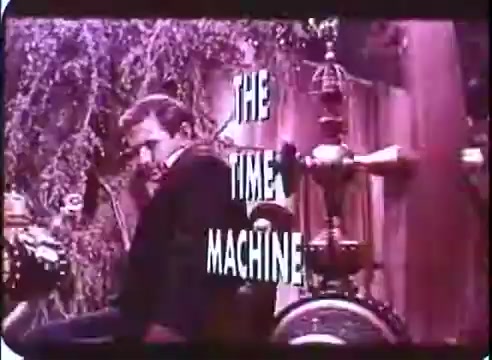 The still features a character seated beside a vintage-looking time machine apparatus, with whimsical and intricate details in the background. The title 'THE TIME MACHINE' is prominently displayed in bold, stylized letters, suggesting a blend of science fiction and adventure. The color tone appears warm, evoking a nostalgic feel typical of 16mm prints.