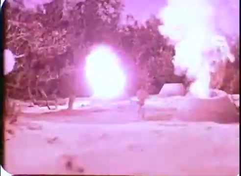 The still from 'The Time Machine' promos features a landscape with vibrant colors, primarily dominated by purples and bright whites. In the foreground, a figure appears to be caught in a scene of action, possibly amidst explosions or bursts of light. Background elements include trees and structures that suggest a fantastical or otherworldly environment, enhancing the sense of adventure and tension typical of sci-fi films from the era. The overall atmosphere conveys excitement and intrigue.