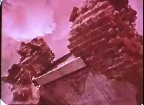 The still from 'The Time Machine' promos showcases a dramatic, perhaps dystopian landscape featuring crumbling brick structures. The colors are heavily filtered, casting a reddish tint over the scene, which enhances the feeling of decay and desolation. The angle suggests a downward view, emphasizing the ruins against a stormy or ominous sky, contributing to the film's themes of time and consequence.
