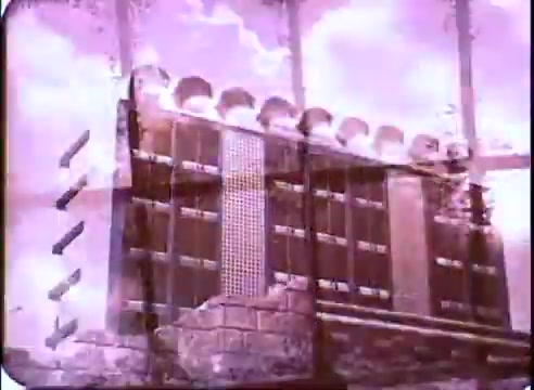 The still from the promotion for 'The Time Machine' features a vintage 16mm print aesthetic, showcasing a mix of architectural elements, possibly depicting a futuristic or advanced structure. The color tone leans towards pink and purple hues, enhancing the surreal and imaginative atmosphere, characteristic of science fiction. The image conveys a sense of time travel or alternate realities, resonating with the film's theme.