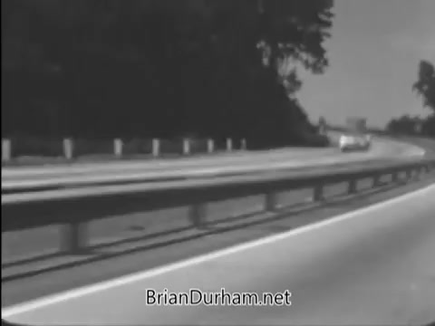 The still from the 1968 PSA titled 'New Guardrails' depicts a highway scene showing a vehicle approaching guardrails designed to slow down cars in the event of a crash. The emphasis is on demonstrating how these guardrails can prevent vehicles from crossing the median and colliding with oncoming traffic, highlighting their life-saving potential. Produced by the Sheet Committees of the American Iron and Steel Institute, the message promotes highway safety through effective infrastructure design.