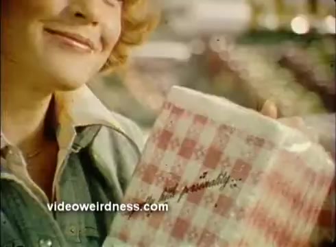 The still features a smiling woman holding a package of Mardi Gras paper products, which showcases a red and white checkered design. The setting suggests a festive atmosphere, likely associated with celebrations. The focus is on the paper products, emphasizing their suitability for special occasions. The overall tone is cheerful and inviting.