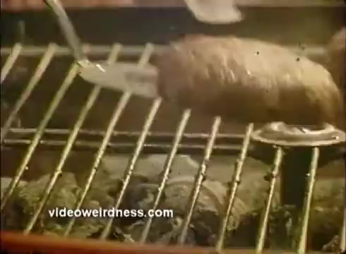 The still depicts a close-up shot of grilled food on a barbecue grill. A utensil is lifting a piece of meat, while several other items are visibly cooking beneath it. The image has a vintage quality typical of 16mm film, capturing the essence of a lively cooking scene likely featured in a Mardi Gras paper products commercial, emphasizing celebration and festive dining.