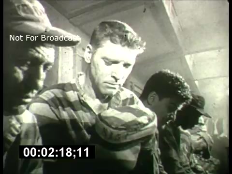 The still is from a 1960s promo for the ABC Sunday Night Movie. It features a group of men in striped attire, possibly depicting a scene from a film about confinement or hardship. The mood appears somber, with the subjects expressing various emotions, likely reflecting themes of struggle or survival. The black-and-white format adds a historical feel, typical of that era's cinematic style. The timestamp indicates it is part of a promotional clip, intended to build interest for Sunday night programming.