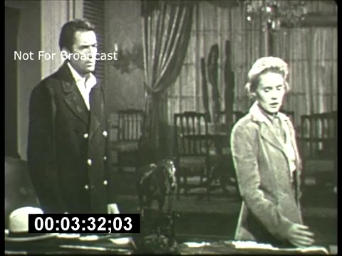 This 16mm still from a 1960s promo for the ABC Sunday Night Movie features two actors in a dramatic scene. The setting appears to be an elegantly furnished room, possibly a living area with a large table and distant furniture visible. The black-and-white format captures a tense moment, with one actor looking off to the side while the other appears engaged in thought or concern. A time code is visible at the bottom, indicating its use for editing or broadcast purposes. The text 'Not For Broadcast' suggests that this is a restricted preview or promotional material.