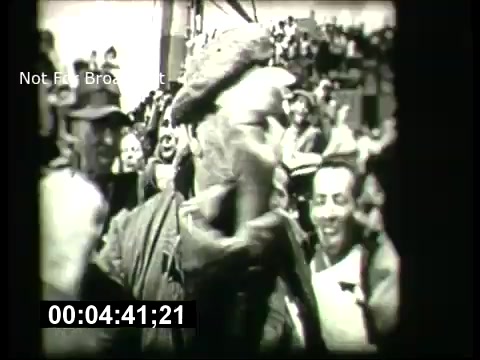 The still from the 'ABC Sunday Night Movie' promos from the 1960s features a crowd scene, with a notable focus on an individual wearing a hat and engaging with the surrounding people. The atmosphere appears lively, with several faces showing excitement or joy. The image is in black and white, capturing the vintage aesthetic typical of that era, and includes a timing stamp indicating the duration.