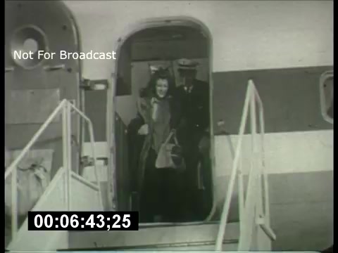 The still from 'ABC Sunday Night Movie promos - 1960s' features a scene where a woman, accompanied by a man in a pilot uniform, is disembarking from an airplane. The photo captures a moment of arrival, likely intended to evoke excitement and anticipation. The monochromatic aesthetic typical of the era contributes to the vintage feel of the promo. The overlay text indicates it's not for broadcast.