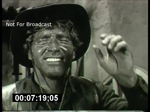 This still from the 'ABC Sunday Night Movie' promos of the 1960s features a smiling, rugged character with a dirty face and a broad-brimmed hat. The character appears cheerful and is gesturing, possibly as part of a lighthearted or comedic moment. The black-and-white imagery reflects the era's film style, adding a nostalgic tone. The time code suggests it's a segment from a specific moment in the promo reel.