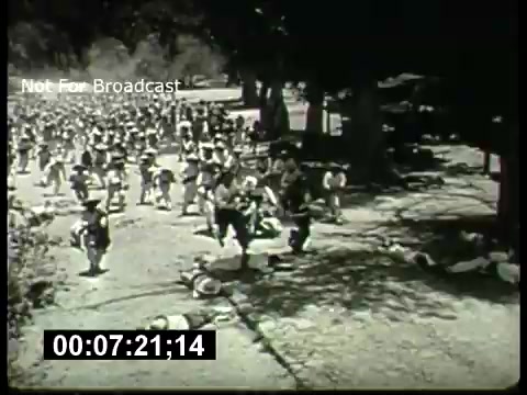 The still from 'ABC Sunday Night Movie promos - 1960's' features a scene depicting a large crowd, possibly in a chaotic or active moment. People are seen moving through a wooded area, suggesting an outdoor setting. The monochrome aesthetic characteristic of 16mm film adds a vintage quality, hinting at the era of the 1960s. The inclusion of the timestamp indicates a clip from a broadcast, emphasizing its promotional context for the ABC network during that period.