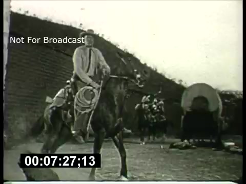 The still from the 'ABC Sunday Night Movie' promos in the 1960s shows a black-and-white scene featuring a cowboy on horseback, likely engaged in a Western-themed moment. The cowboy is dressed in traditional attire with a lasso, suggesting an adventurous narrative, while a covered wagon and several figures in the background hint at a larger story involving a frontier setting. The image carries a vintage aesthetic typical of that era's film promotions.