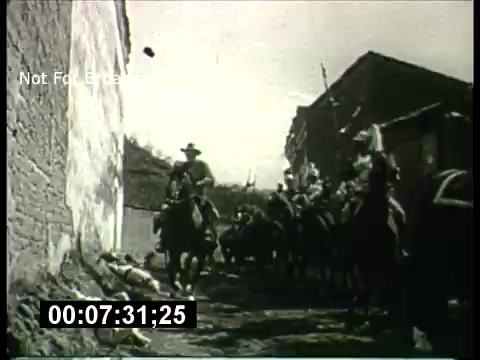 The still from the 'ABC Sunday Night Movie promos - 1960's' features a black-and-white scene depicting a group of mounted figures, likely representing a cavalry or armed procession, riding through a narrow street lined by buildings. The atmosphere suggests a historical or cinematic context, possibly hinting at an action or adventure theme typical of that era's movie promotions. The overall composition includes visible elements such as a wall and the ground, contributing to a sense of depth. A time code is also present at the bottom, indicating the specific moment in the film segment.