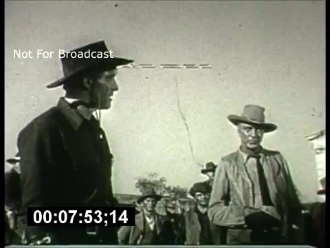 The still features a scene from a 1960s ABC Sunday Night Movie promo. It depicts two men in cowboy attire engaged in a tense conversation, surrounded by a group of onlookers. The black-and-white format gives it a classic feel, typical of the era’s television productions. A digital timer in the corner indicates the duration, while a watermark states it is 'Not For Broadcast.' The dramatic setting suggests themes of conflict or confrontation, common in western films of the time.