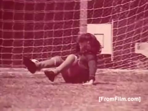 The still features a young child on a soccer field, having fallen near a goal post. The image captures a playful, candid moment, emphasizing the joy and innocence of childhood activities. The color tone appears warm and vintage, characteristic of 1970s film stock. This scene likely aims to convey a sense of comfort and nostalgia associated with family meals, reinforcing the presence of Knorr Caldo De Galinha soup in everyday life.