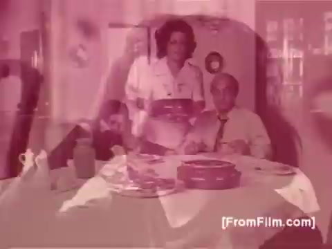 The still from the Knorr Caldo De Galinha soup commercial features a dining scene set in a cozy, home-like environment typical of the 1970s in Brazil. A woman, likely a homemaker, is serving a dish to a seated man, who appears pleased. The scene conveys warmth and family togetherness, highlighting the product's role in enhancing mealtime. The color tones suggest a vintage look consistent with 16mm film quality from that era.