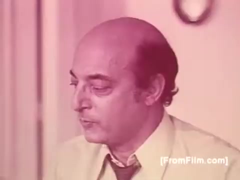 The still from the 1970s Knorr Caldo De Galinha soup commercial features a middle-aged man with a bald head, wearing a light-colored shirt and tie. His expression seems thoughtful or contemplative, suggesting he might be reflecting on a moment related to the soup. The color tone of the print appears warm, characteristic of the time, and the setting looks casual, likely depicting a domestic environment.