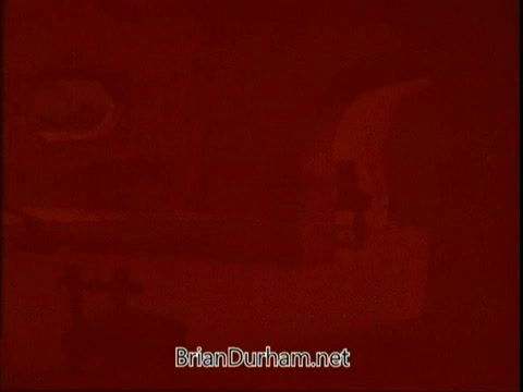 The still appears to be a faded or improperly exposed frame from a 16mm film of the 'Flintstones American Cancer Society PSA.' The dominant red hue obscures details, making it hard to discern specific elements. The image includes text at the bottom linking to BrianDurham.net, possibly indicating the source or related content.