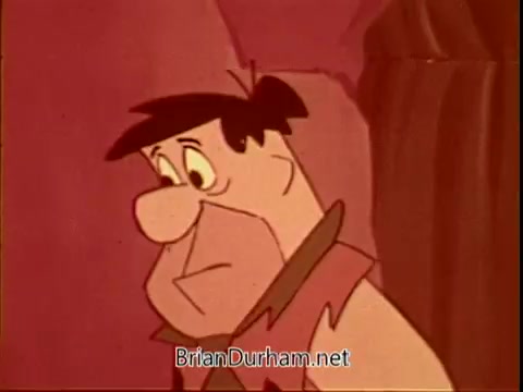 The still features Fred Flintstone, portrayed with a somber expression. The colors are warm, leaning towards orange and pink, reflecting the vintage animation style. This image is from a PSA for the American Cancer Society, aiming to convey a serious message through the familiar character design.