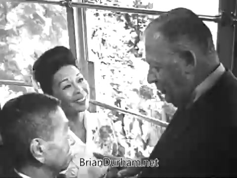 The still features a scene from the 'Rolaids Commercial,' showcasing a conversation among three individuals: a man and a woman, both smiling, and another man attentively engaged in the discussion. The setting appears cheerful and inviting, with foliage visible outside a window, adding a bright, natural backdrop. The overall tone suggests a lighthearted endorsement of Rolaids, emphasizing its effectiveness against stomach acid.