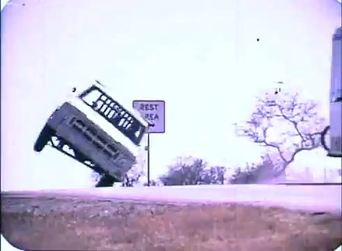 The still from the trailer of 'Race with the Devil' features a vehicle dangerously tilting on a rural road, likely in a moment of high tension or a chase. A 'Rest Area' sign is visible, hinting at a roadside location. The bright colors and the 16mm print capture a sense of urgency and peril characteristic of the film's themes.