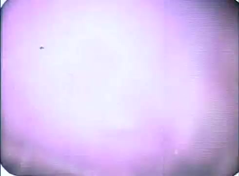 The still from the trailer of 'Race with the Devil' features a hazy, washed-out background with a subtle purple tint. The image appears to be slightly out of focus, creating a dreamlike quality, and there is a small object in the upper left corner, likely indicating movement or action. The overall impression is one of tension, characteristic of the horror-thriller genre.