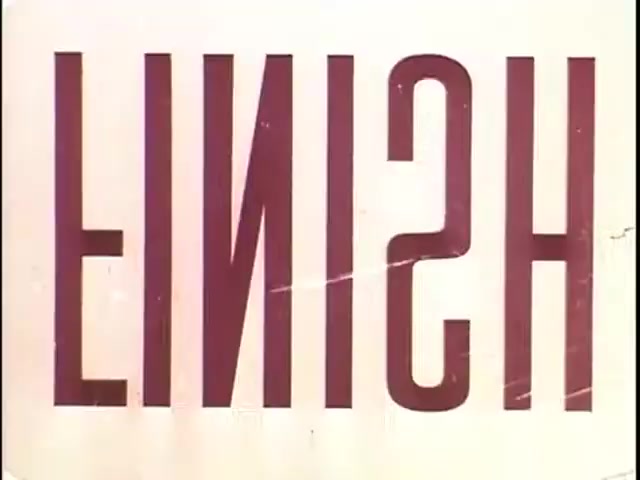 The still features the word 'FINISH' prominently displayed, rendered in bold, stylized typography. The text is oriented in a way that makes it appear upside down. The background is a plain color, likely cream or light beige, adding to the simplicity of the design. There are visible marks or scratches, suggesting wear from the 16mm film medium. This still likely serves as a visual cue in the context of tape-to-film transfers, particularly from commercials.