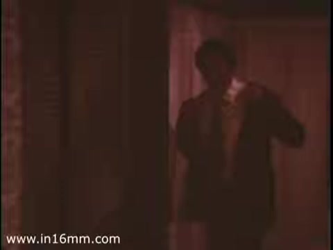 The still from the 16mm print of 'Sole Leather Council Bicentennial PSA - 1975' depicts a man in a suit appearing to walk out of a dimly lit area. The overall color tone is warm, possibly hinting at an indoor setting. The message emphasizes using shoes for transport to save gas, contrasting traditional methods with a call for more eco-friendly practices.