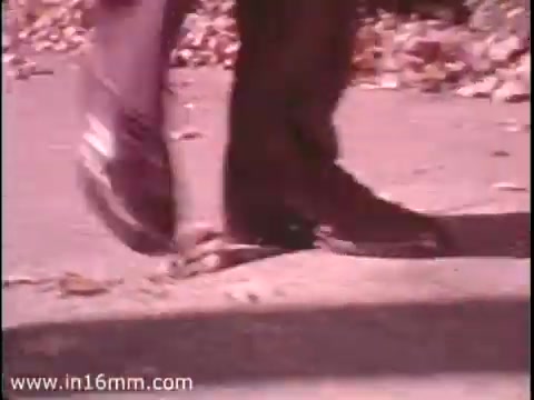 The still features a close-up of a person's shoes walking on a pavement, emphasizing the theme of utilizing personal energy over vehicles. It's a scene promoting the idea of saving gas by encouraging walking, tied to the Sole Leather Council's bicentennial message in 1975. The image captures a sense of movement, suggesting a practical and eco-friendly lifestyle.