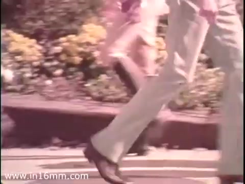 The still from the 1975 'Sole Leather Council Bicentennial PSA' features individuals walking along a sidewalk, emphasizing a message about saving gas by using shoe leather instead. The color palette is warm and retro, typical of the era's aesthetic. The focus is on footwear and movement, promoting the idea of walking as an eco-friendly transportation alternative.