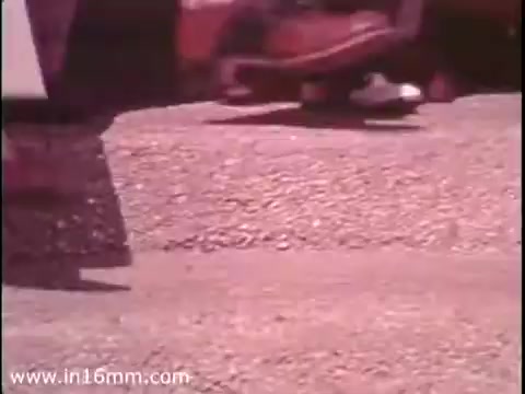 The still from the 'Sole Leather Council Bicentennial PSA - 1975' shows a close-up of a person's foot in a casual shoe, possibly stepping on a gravel or asphalt surface. The PSA conveys a message encouraging people to “save gas” by promoting walking instead of driving. The vintage aesthetic typical of a 16mm print adds a nostalgic feel to the imagery.