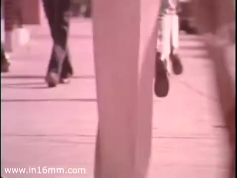 The still from the 'Sole Leather Council Bicentennial PSA - 1975' features a close-up view of feet walking on a sidewalk, emphasizing the theme of using walking ('shoe leather') as an alternative to driving. The motion suggests activity and promotes a message of saving gas through pedestrianism. The colors appear warm, typical of the era’s film style.