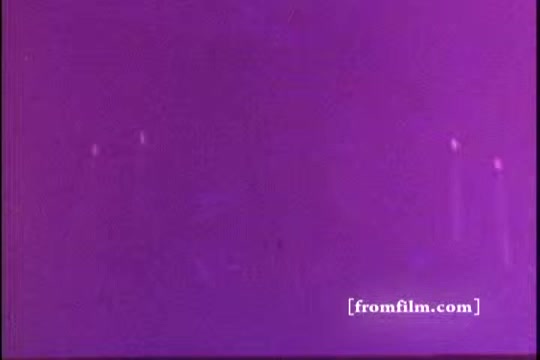 The still from 'Vanity Fair Napkins - 1970's' features a vivid purple background with indistinct shapes or highlights, likely due to the aging process of the 16mm print. The overall composition is abstract, creating a dreamy or surreal atmosphere. The image lacks clear details, emphasizing color and texture.